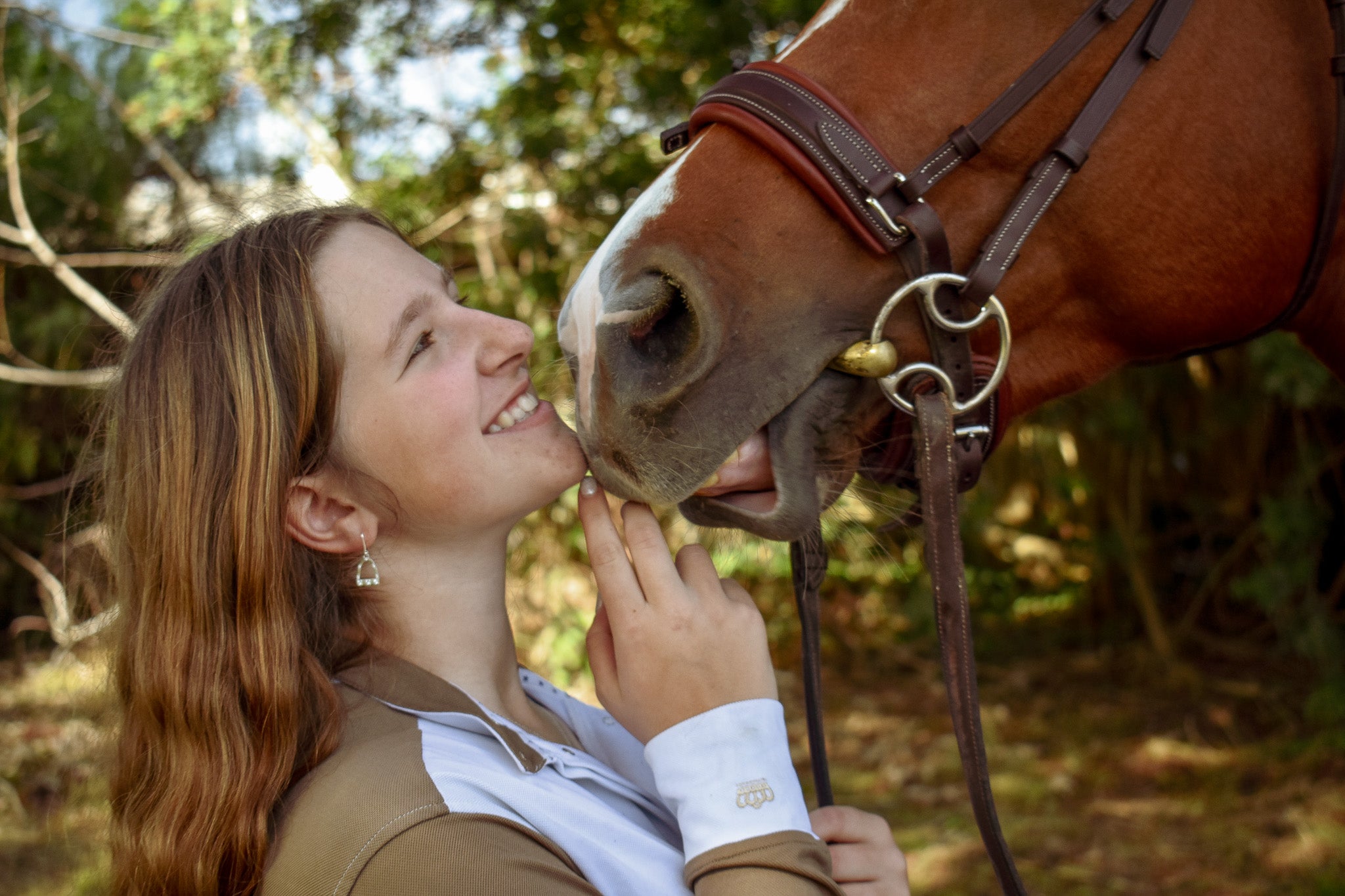 Close up of a model wearing the stirrup lariat earrings while touching her nose to a horse nose