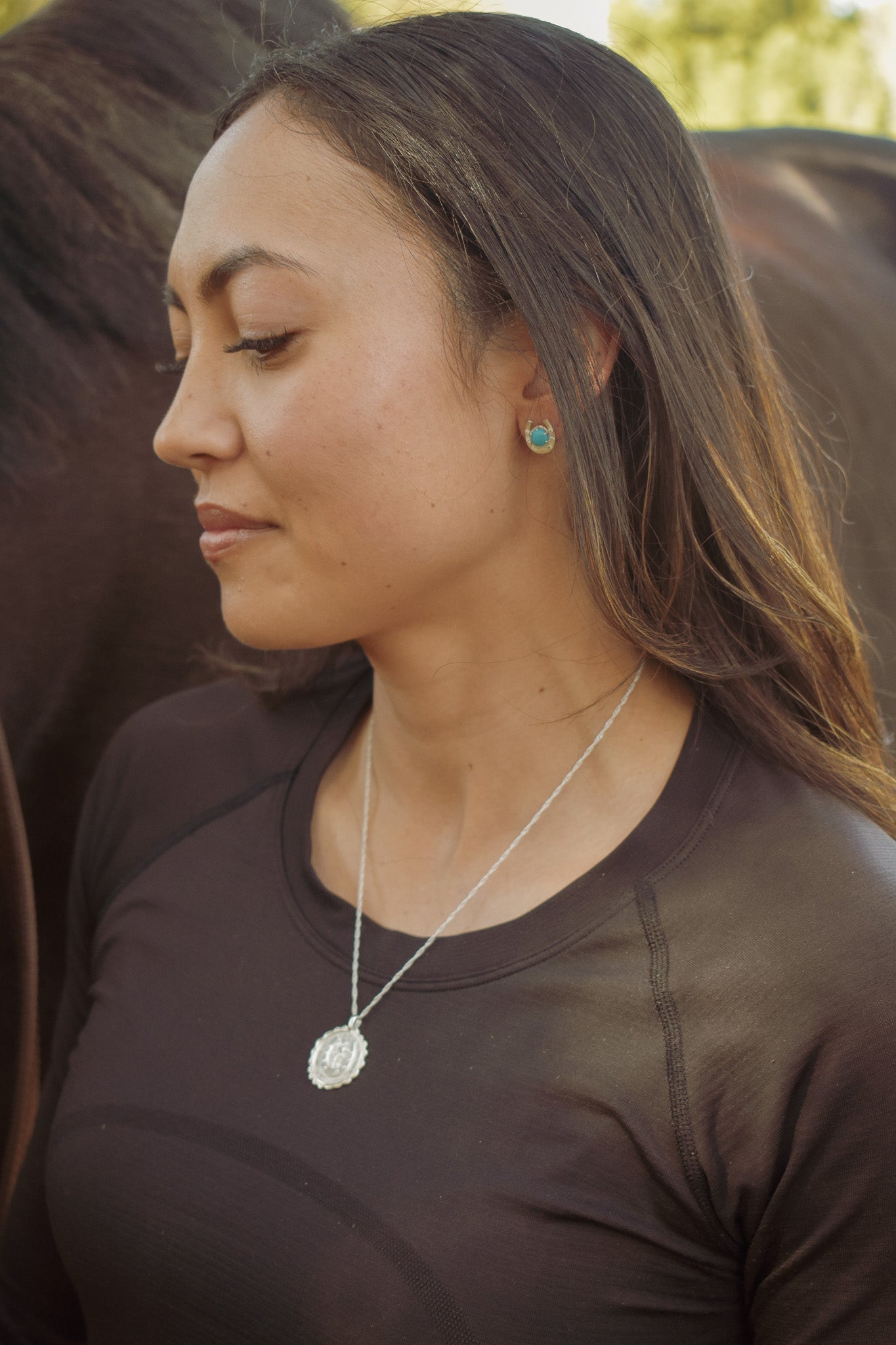 Model smiling, looking down while wearing turquoise good luck studs and sterling silver good luck amulet