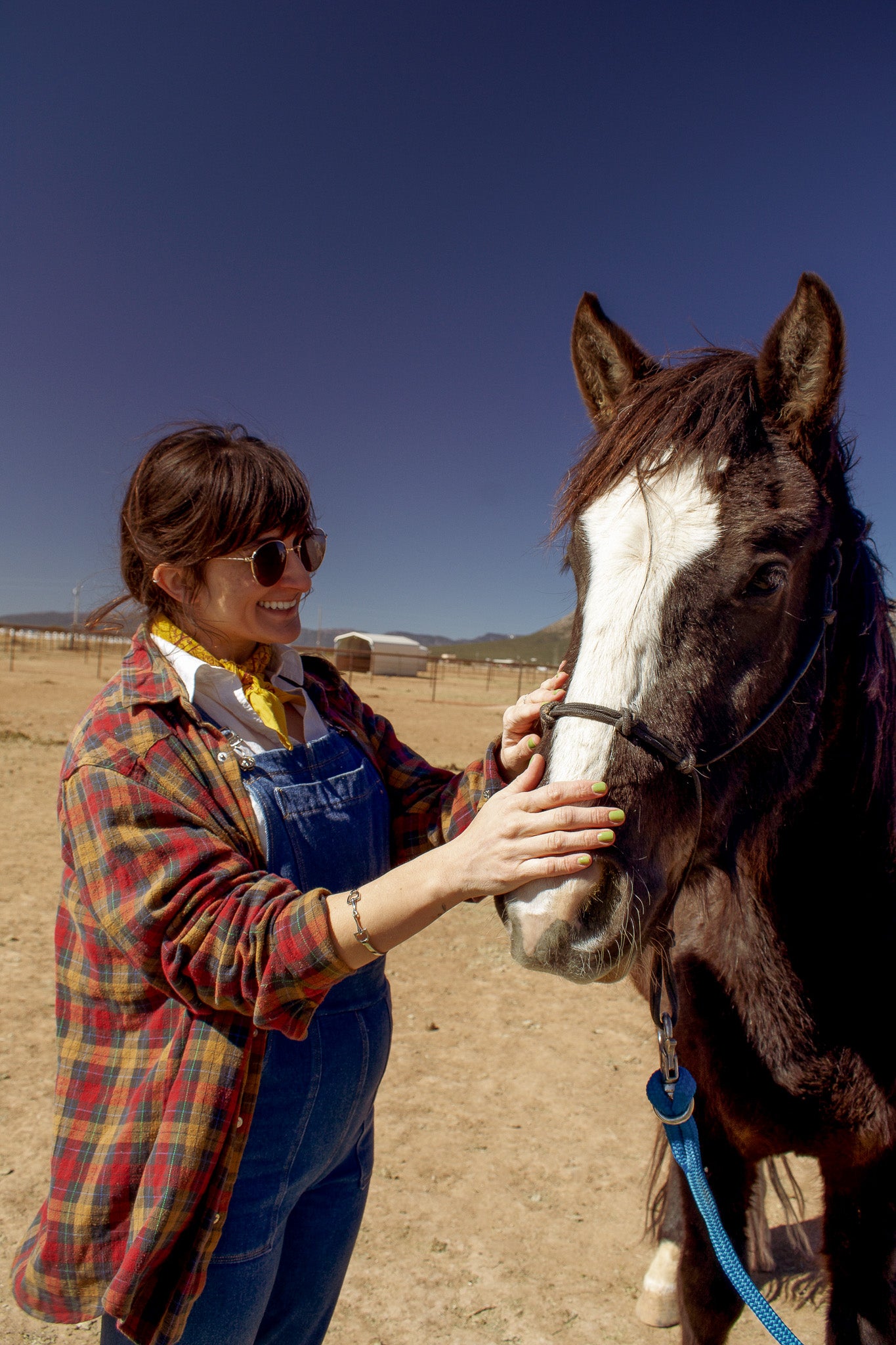 Model wearing the bit bandle, smiling and petting the horse at a barn