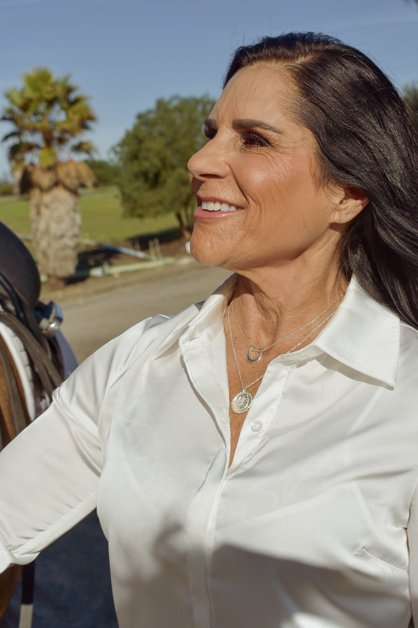 Model in white silk blouse wearing the sterling silver horseshoe pendant and good luck amulet with trees in the background