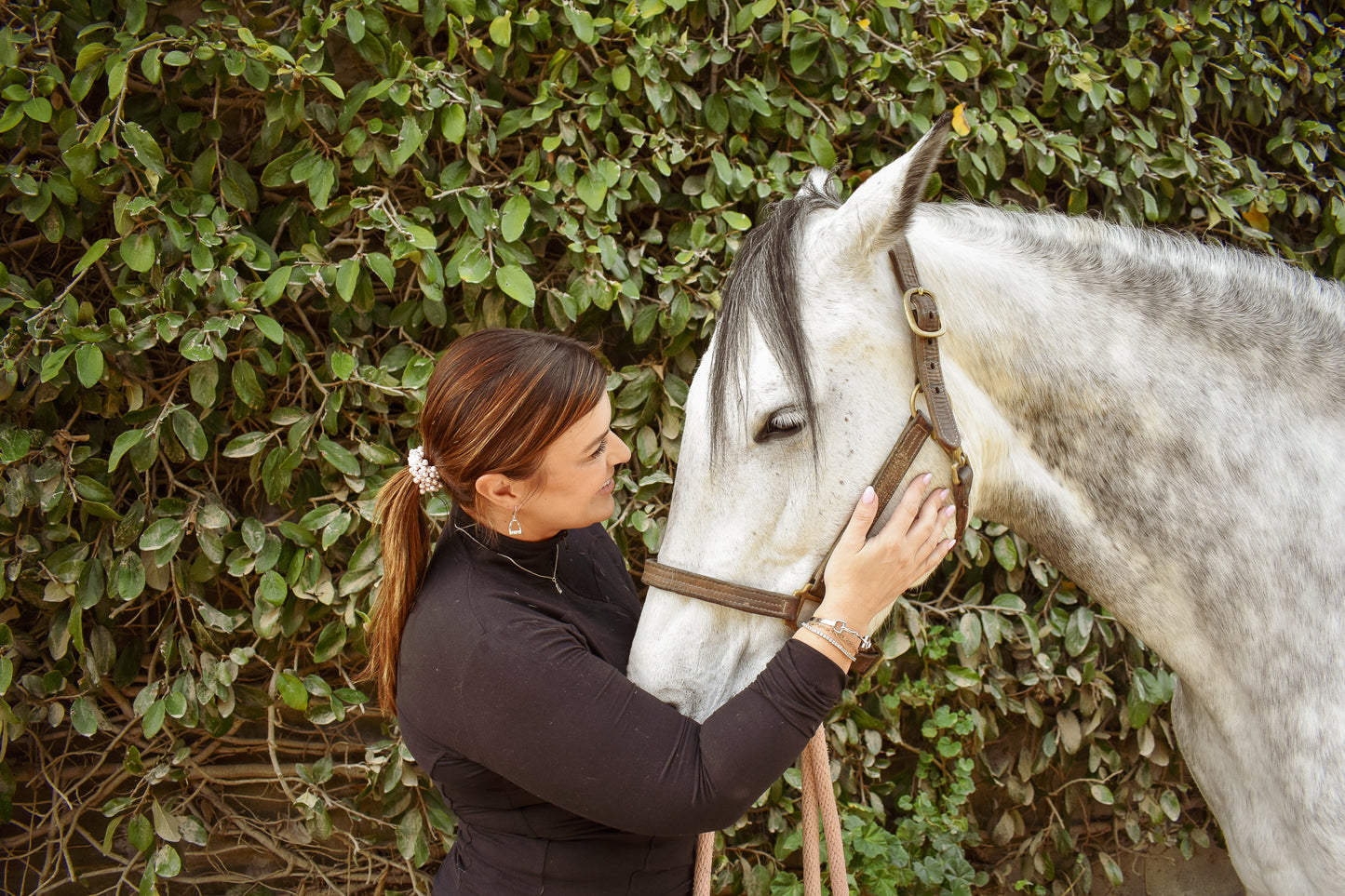 model wearing the sterling silver stirrup lariat necklace with matching earrings, smiling and petting her horse