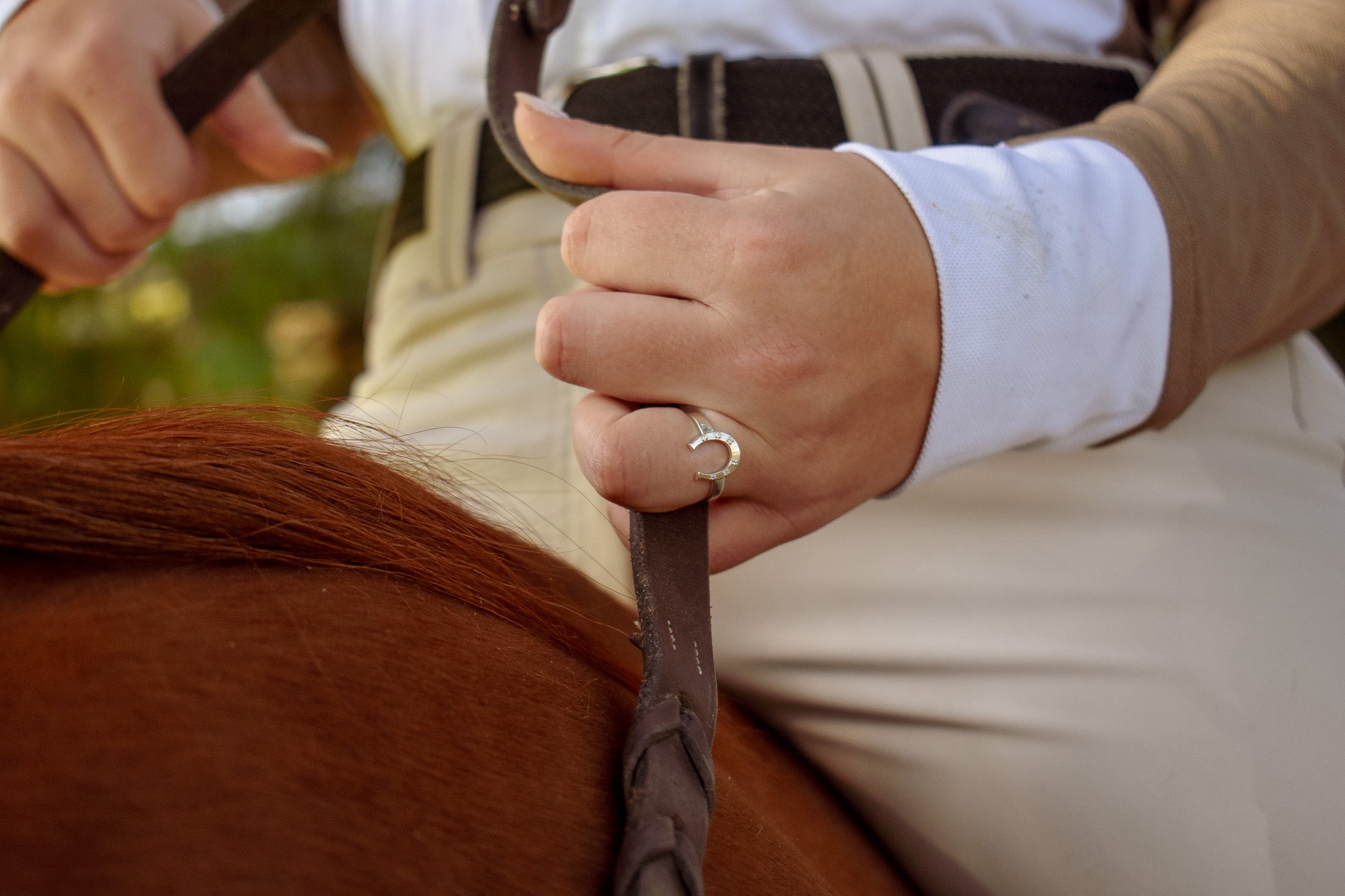 Model sitting on her horse, holding her reins with a close up on the sterling silver horseshoe ring